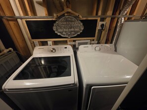 A laundry room with two Samsung washers and dryers, a self-service sign, and a 24-hour service notice.