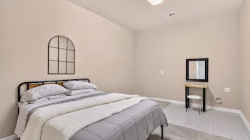 Un dormitorio con cama, mesita de noche, espejo y ventana con diseño de cuadrícula.