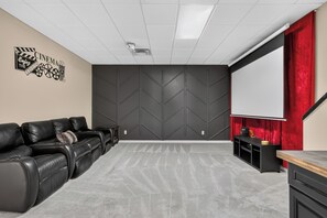 A home theater room with a black leather couch, a large screen, and a red curtain.