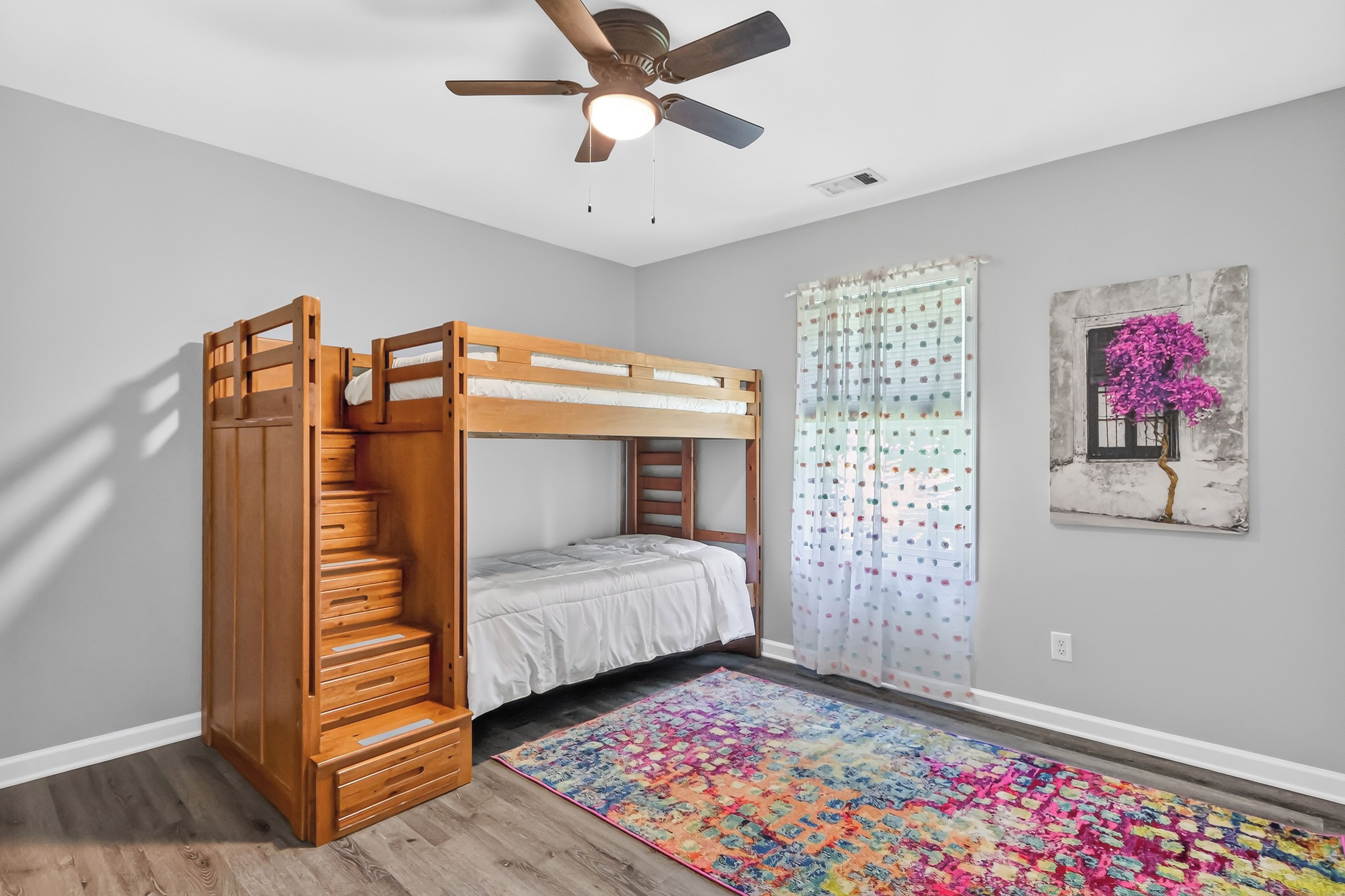A bunk bed room with a ceiling fan, a colorful rug, and a painting on the wall.