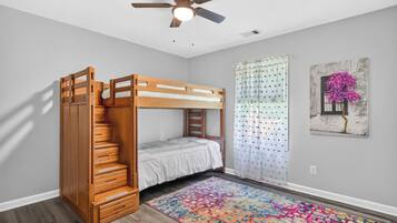 A bunk bed room with a ceiling fan, a colorful rug, and a painting on the wall.