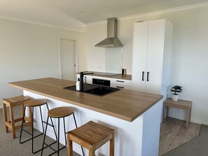 Una cucina moderna con isola centrale, sgabelli da bar, forno integrato e mobili bianchi.