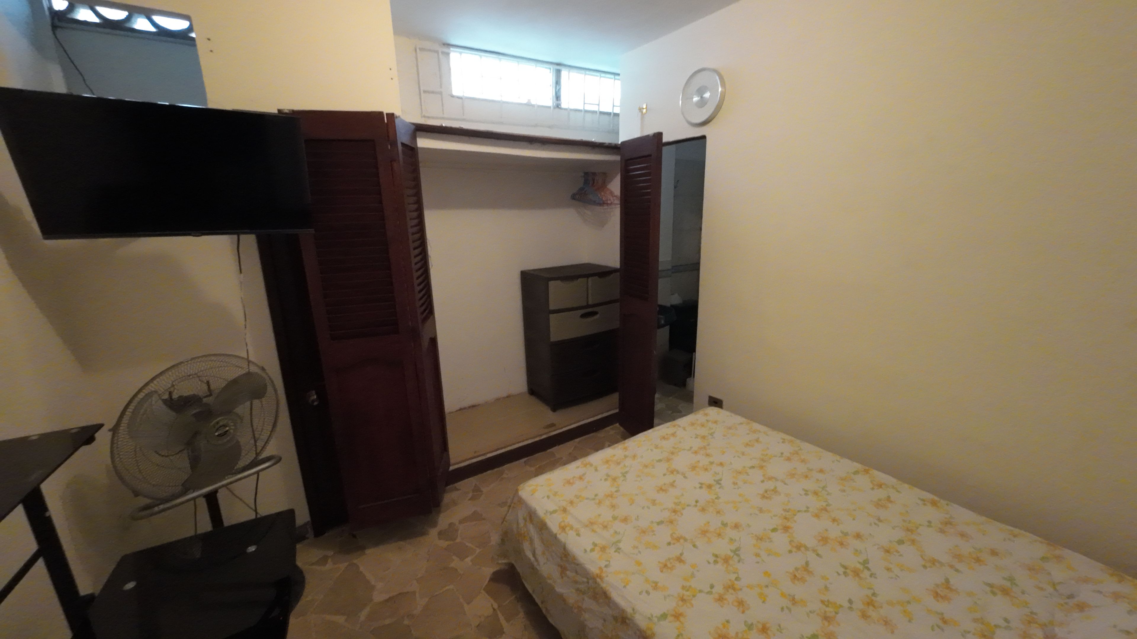 A bedroom with a bed, a fan, a wardrobe, and a television.
