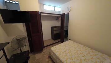 A bedroom with a bed, a fan, a wardrobe, and a television.
