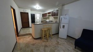 Una cocina con piso de piedra, taburetes de madera, un refrigerador y un reloj en la pared.