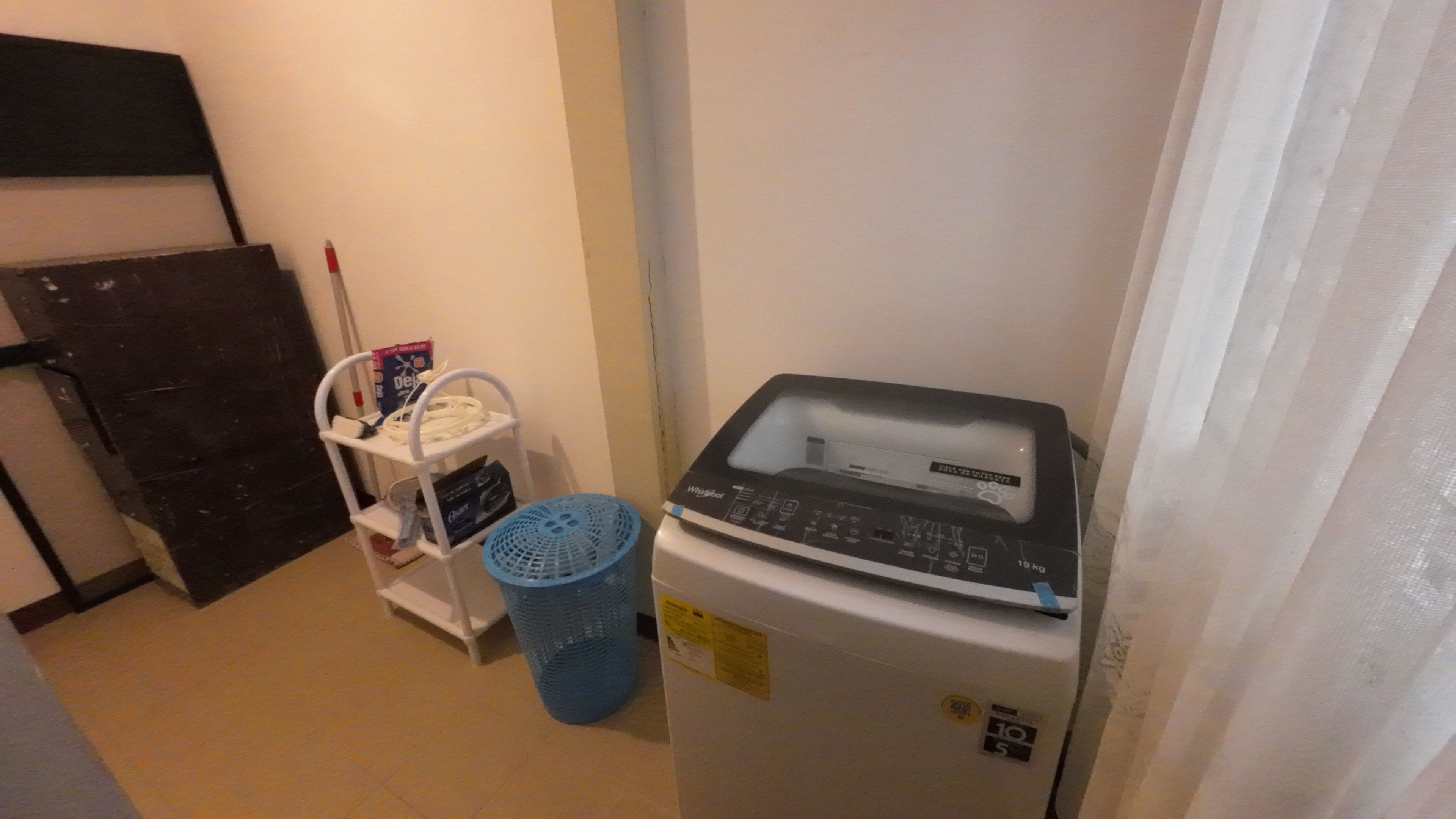 A compact room with a refrigerator, a small shelf with cleaning supplies, and a blue laundry basket.