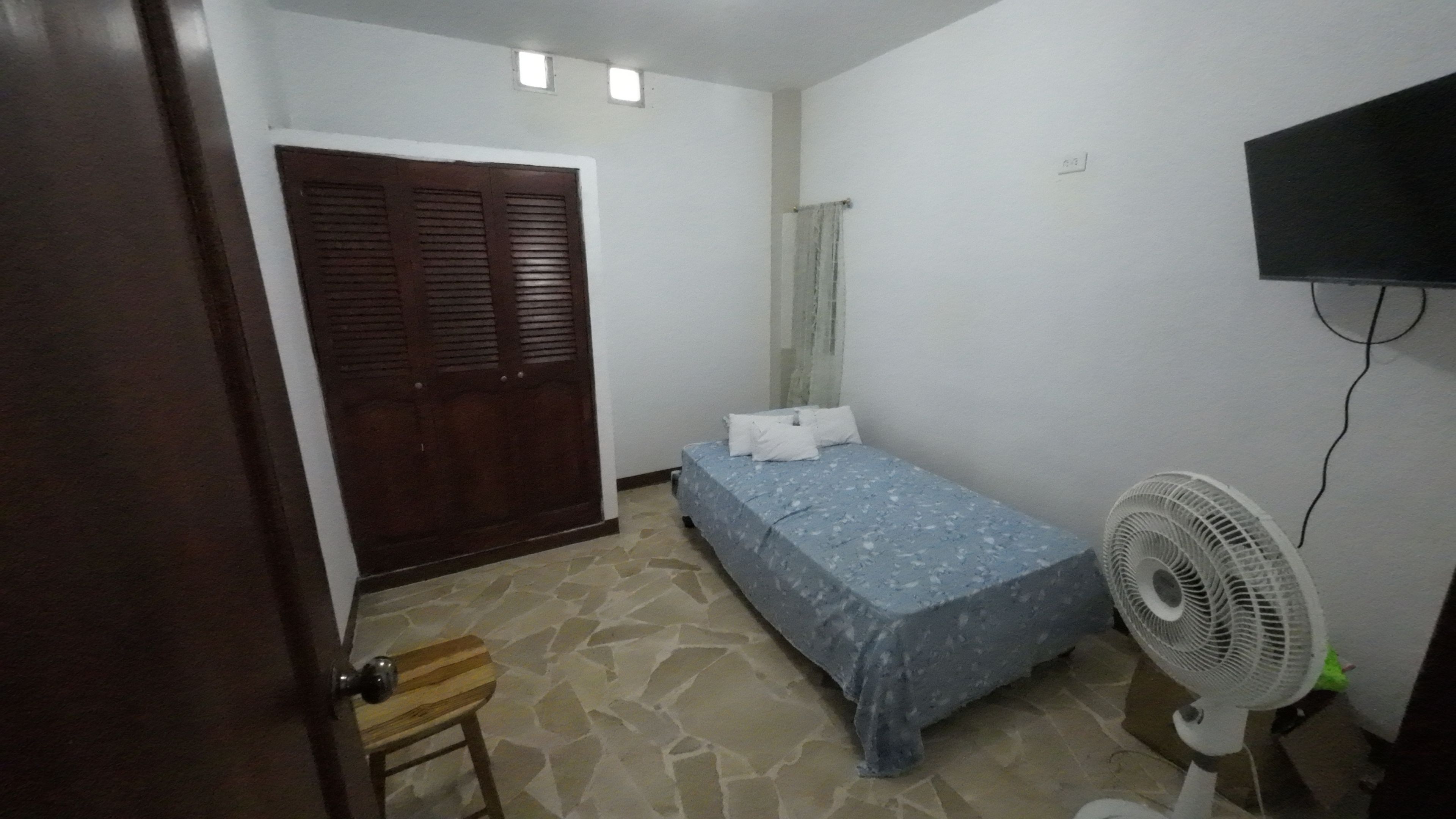 Ein Schlafzimmer mit Bett, Ventilator, Holzschemel und Kleiderschrank.