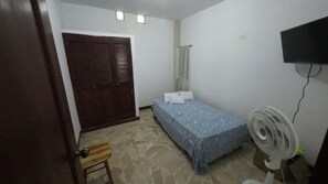 A bedroom with a bed, a fan, a wooden stool, and a wardrobe.