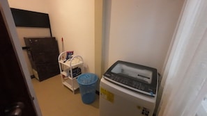 Un lavadero pequeño con una lavadora Whirlpool, un cesto azul para ropa y un estante con varios objetos.