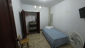 Un dormitorio con una cama, un aparador, una silla, un ventilador y una televisión en la pared.