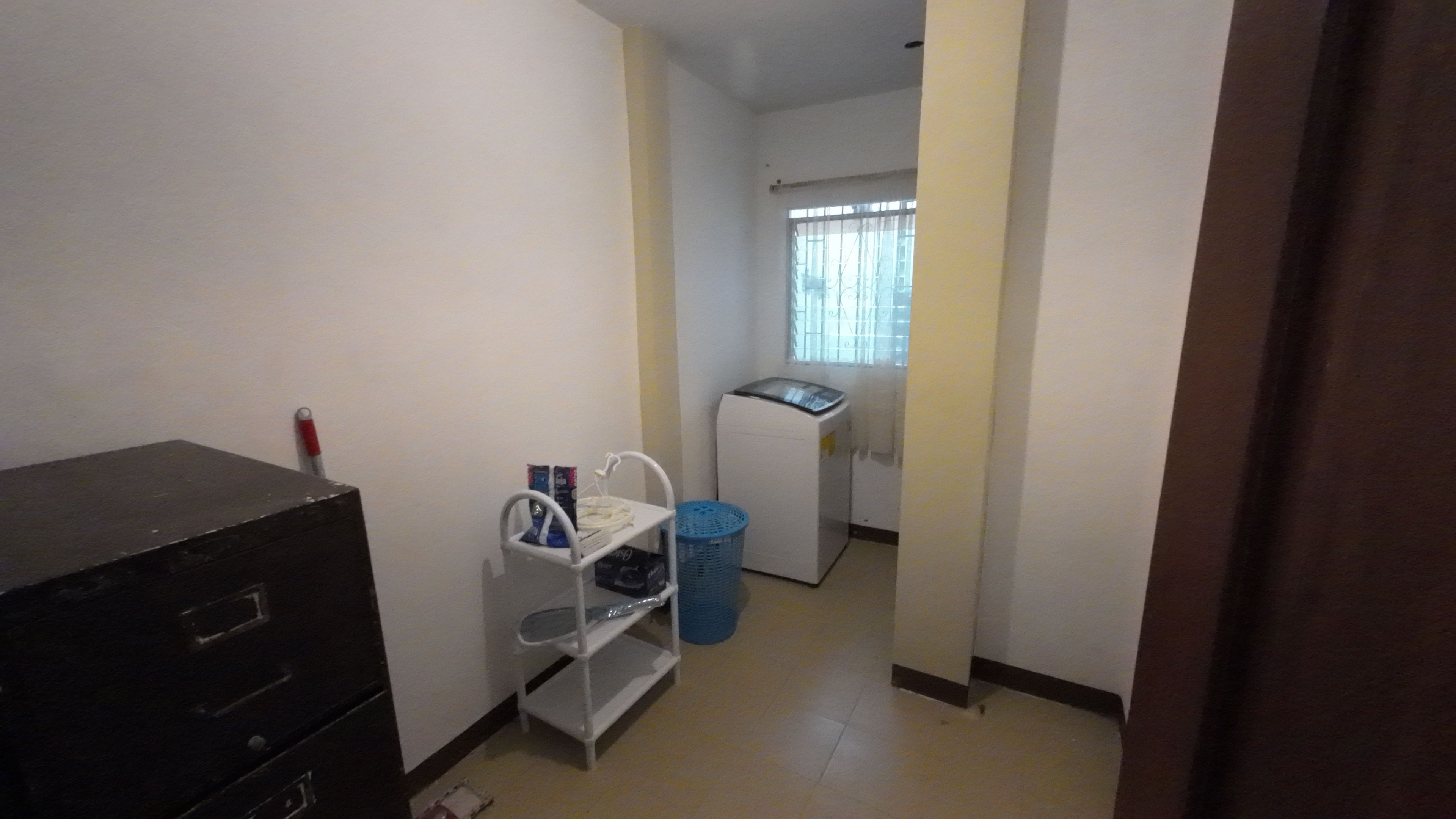 A small laundry room with a washing machine, a drying rack, and a blue laundry basket.