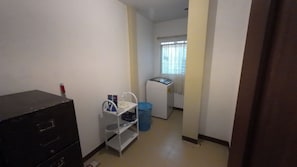 A small laundry room with a washing machine, a drying rack, and a blue laundry basket.
