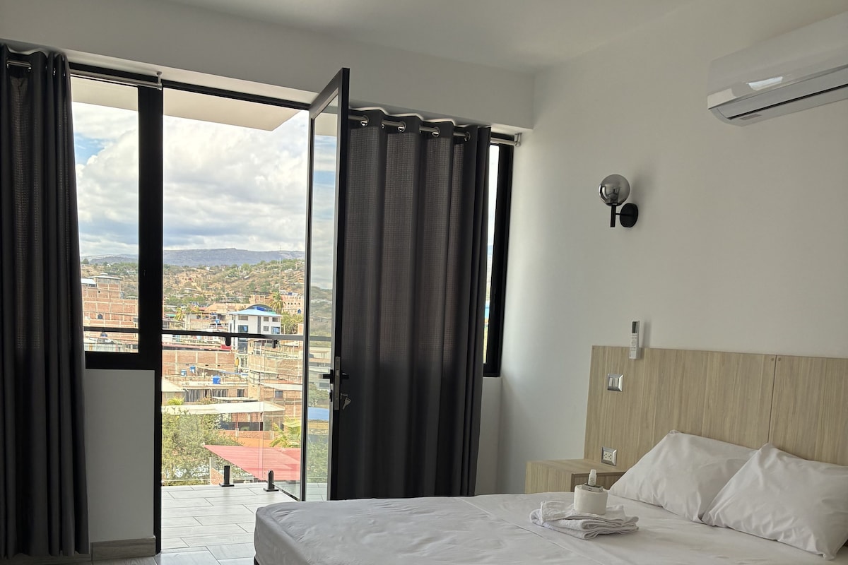 A hotel room with a bed, a view of a cityscape, and a sliding door.