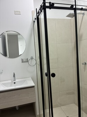 A bathroom with a glass-enclosed shower, a round mirror, and a white sink. - Rego Premium Apart Hotel (Bagua Grande)