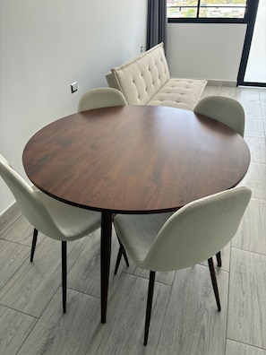 A round wooden table with four chairs, a tufted sofa, and a view of buildings through a window. - Rego Premium Apart Hotel (Bagua Grande)