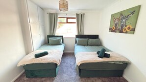 Ein Zimmer mit zwei Betten, einem Vorhangfenster, einer Pendelleuchte und einem Bild an der Wand.