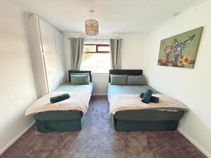 Ett rum med två sängar, ett fönster med gardiner, en hängande lampa och en tavla på väggen.