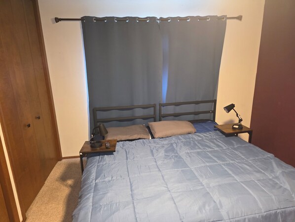 A bedroom with a bed, a nightstand, a lamp, and a curtain.