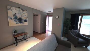 Een woonkamer met een bank, fauteuils, een salontafel, een schilderij, een klok en een plant.