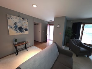 Ein Wohnzimmer mit einer Couch, Sesseln, einem Couchtisch, einem Gemälde, einer Uhr und einer Pflanze.