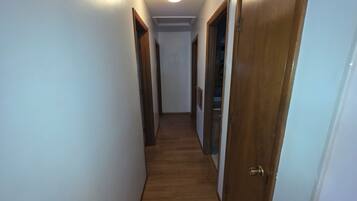 Un pasillo estrecho con suelo de madera y paredes blancas, que conduce a un armario con puerta a la derecha.