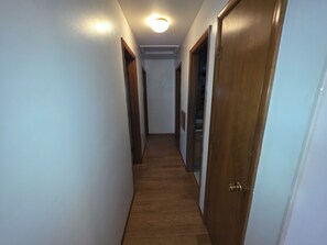 A narrow hallway with wooden flooring and white walls, leading to a closet with a door on the right.