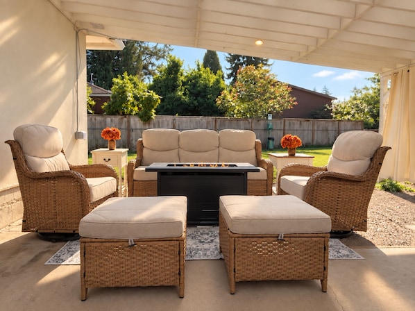 An outdoor patio with wicker furniture, a central table, and a fire feature.