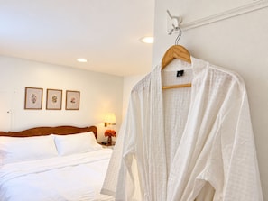 A hotel room with a bed, a wooden headboard, and a white robe hanging on a hook.