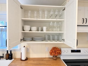 A kitchen with open cabinets containing dishes, glasses, and a vase with flowers.