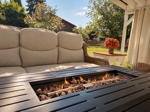 A patio with a metal fire pit, a beige sofa, and a small table with a vase of flowers. - Bluebell Cottage, Walkable Fall City Stay w/ Hot Tub & Fenced Yard, Pets Welcome (Fall City)