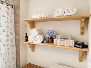 A bathroom with wooden shelves holding towels, a bottle of lotion, a potted plant, and a box with the text 'Just incase.' - Bluebell Cottage, Walkable Fall City Stay w/ Hot Tub & Fenced Yard, Pets Welcome (Fall City)