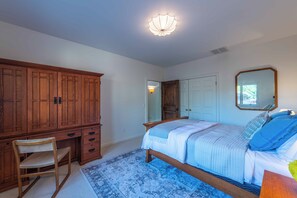 A bedroom with a wooden wardrobe, a bed with blue bedding, a chair, and a patterned rug. - Gorgeous 5BR Spanish Villa w/Pool & Spa in Paso Wine Country (Paso Robles)