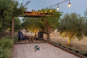 An outdoor patio area with a pergola, two Adirondack chairs, a table, and a scattering of colorful balls on the ground. - Gorgeous 5BR Spanish Villa w/Pool & Spa in Paso Wine Country (Paso Robles)