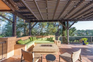 Eine Terrasse im Freien mit einem grünen Sofa, zwei Korbstühlen, einem runden Tisch und einem Feuerkorb.