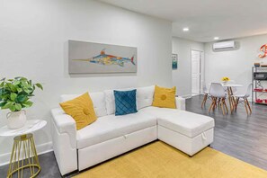 A modern living room with a white sectional sofa, a painting of a fish, and a dining area with chairs and a table. - 3 minutes from pleasure pier near beaches (Galveston)