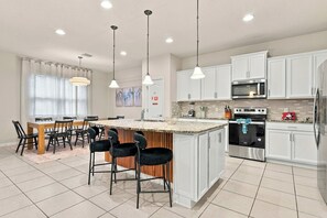 A modern kitchen with white cabinets, a central island with bar stools, stainless steel appliances, and pendant lighting. - 2472 Toy Barn Slide Bed & Game Room! Private Pool (Kissimmee)