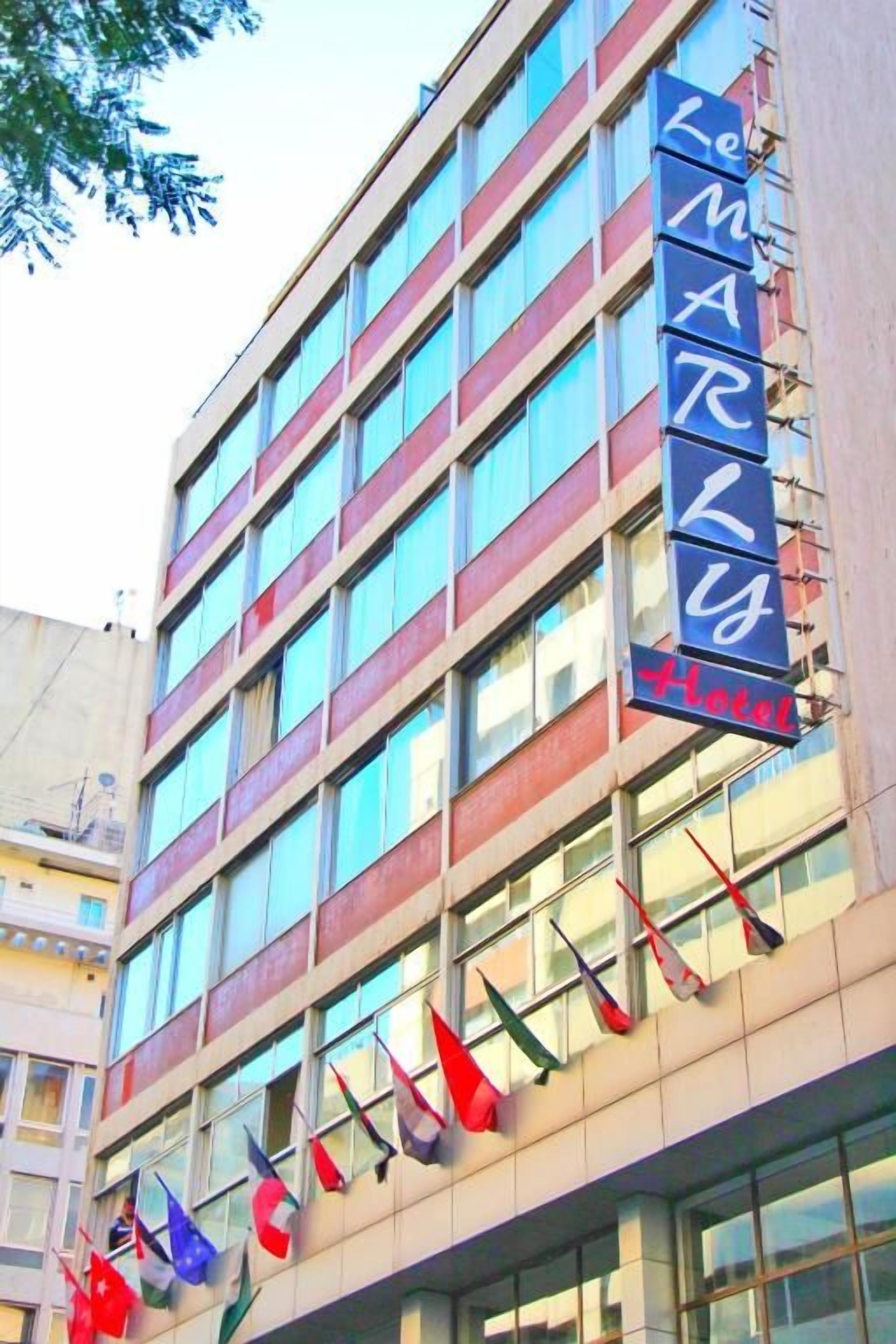 Un edificio de varios pisos con un letrero vertical que muestra el nombre 'Hotel L'Amer' y varias banderas colgadas en las ventanas.