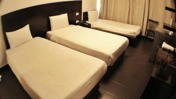 A hotel room with two single beds, a dark headboard, a nightstand, a chair, and a desk with a lamp.