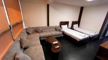 Habitación de hotel compacta con sofá, dos camas individuales, una mesita y cabecero de madera.