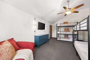 Ein Schlafsaalzimmer mit Etagenbetten, einer blauen Kommode, einem Fernseher und einem Deckenventilator.