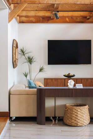Ein Wohnzimmer mit einer Couch, einem Couchtisch, einem an der Wand montierten Flachbildfernseher, einem Zier-Spiegel und einem gewebten Korb.
