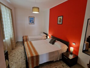 A hotel room with two beds, a red accent wall, a framed picture, a nightstand with a lamp, and a mirror. - Cozy apartment in the heart of Trapani's historic center, near the harbor (Trapani)