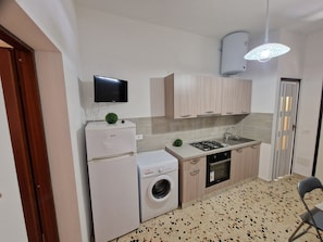 A compact kitchen with a washing machine, a stove, and a TV mounted on the wall. - Cozy apartment in the heart of Trapani's historic center, near the harbor (Trapani)