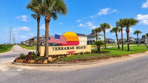 Señal de Terramar Beach con una bandera estadounidense, palmeras y una carretera que lleva a una zona residencial.