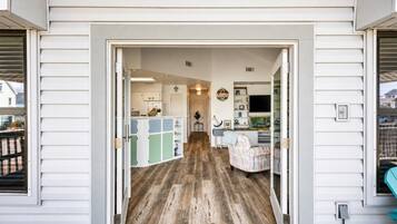 Un corridoio che conduce a una cucina con pavimento in legno, una zona pranzo con tavolo e sedie, e un soggiorno con TV e mensole.