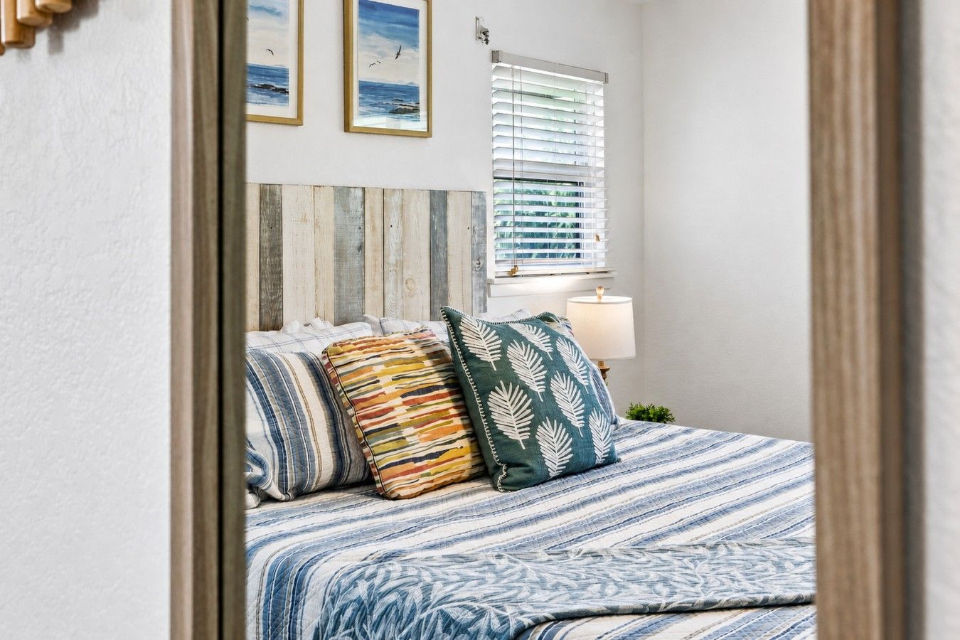 A bedroom with a bed, pillows, a bedside lamp, and a window with blinds.