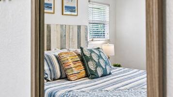 A bedroom with a bed, pillows, a bedside lamp, and a window with blinds.