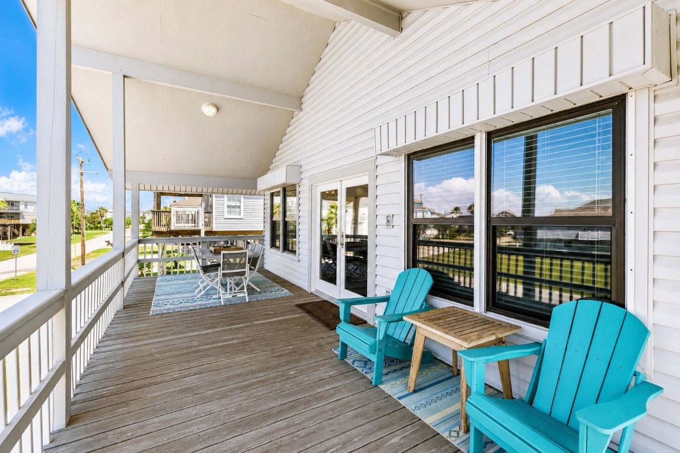 A covered porch with a wooden deck, outdoor seating, and large windows.