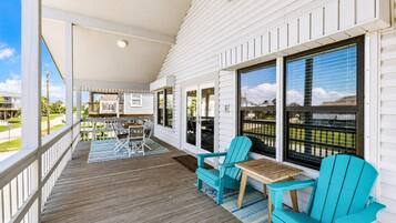 A covered porch with a wooden deck, outdoor seating, and large windows.