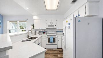 Una cocina moderna con armarios blancos, horno empotrado, refrigerador y ventana con persianas.